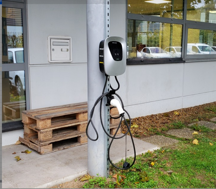 Outdoor installation of a Pilot X Piwin AC EV Charger mounted on a column outside a commercial building, with the charging cable neatly hung.