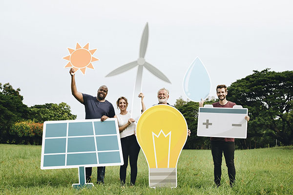 Group of diverse people holding renewable energy icons including solar panel, sun, wind turbine, water drop, light bulb, and battery in a green field.
