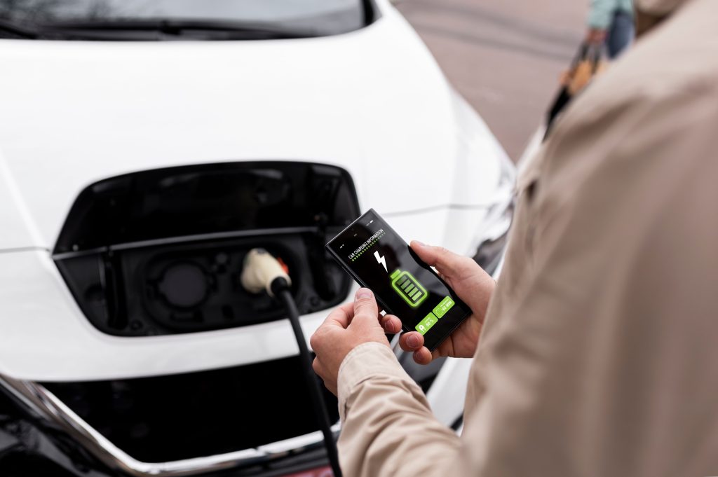 A man is holding his mobile phone to check the charging status of an electric vehicle.