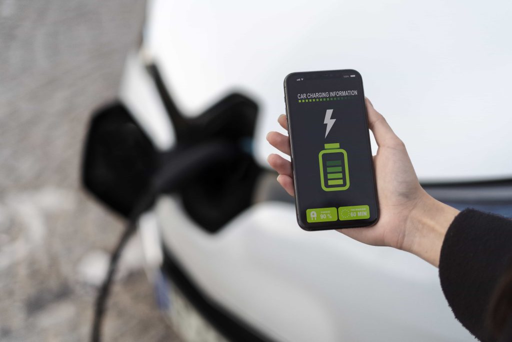 An electric car owner holds up his mobile phone to check the battery capacity of his electric vehicle.