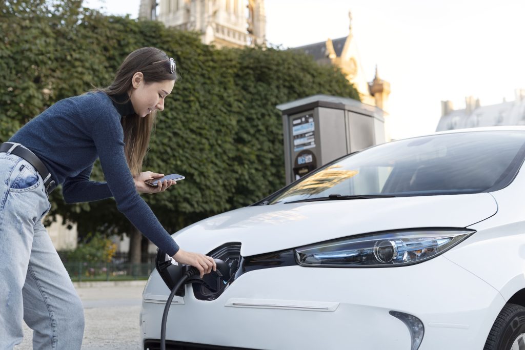 A woman holds an electric car charger in front of her home as she prepares to charge an electric car.